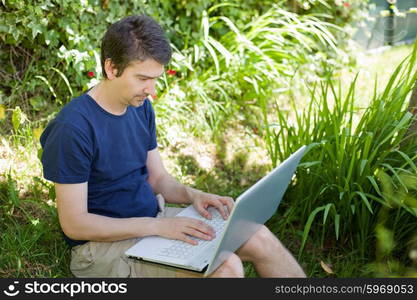 man sitting on the grass working with a laptop