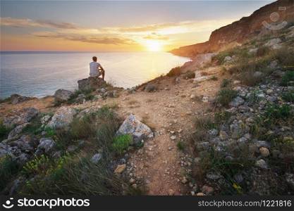 Man sitting on the rock cliff in mountain and watching on thr sunrise sea. Nature composition.