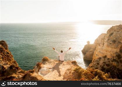 Man sitting on the rocks with open arms to the ocean view - Sunset light