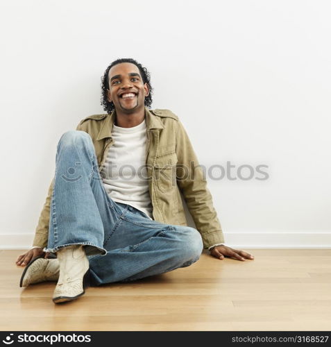 Man sitting on wood floor of home smiling.