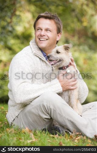 Man sitting outdoors with dog in park smiling (selective focus)