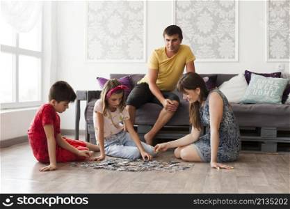 man sitting sofa looking his wife children playing jigsaw puzzle home