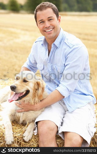 Man Sitting With Dog On Straw Bales In Harvested Field