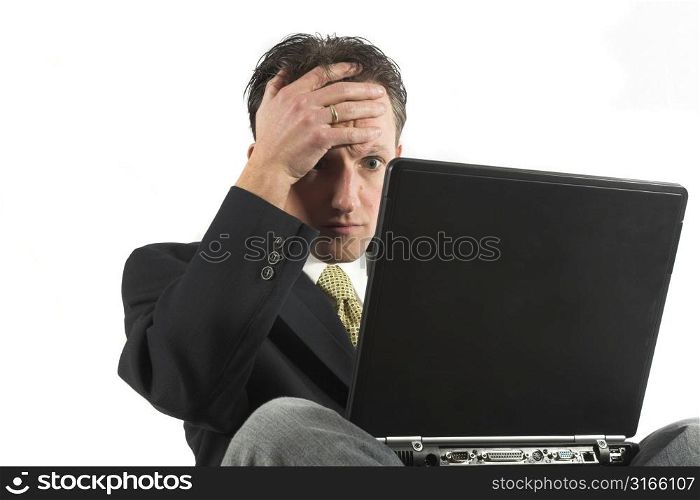 Man sitting with laptop on his lap, looking stressed at the news on his computer