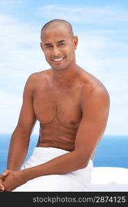 Man sitting with towel round waist smiling half length ocean behind