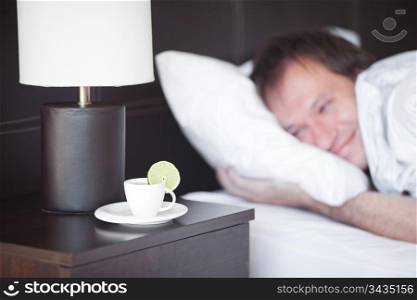 man sleeping on a bed, a cup of tea on the bedside table and lamp
