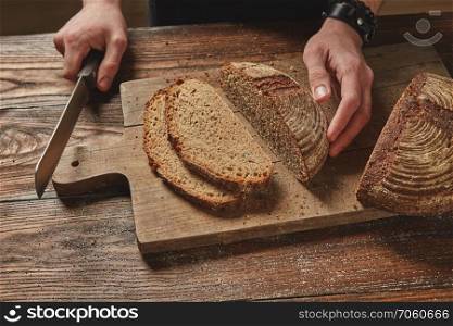Man slicing tasty fresh Rye grain bread. Healthy eating concept. Man slicing tasty fresh bread.