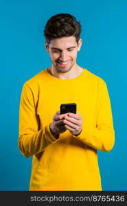 Man sms texting using app on smartphone. Handsome young guy surfing internet with mobile phone. Blue studio background.. Man sms texting using app on smartphone. Handsome young guy surfing internet with mobile phone. Blue studio background