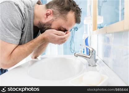Man splashing water on his face, washing himself, taking care of personal hygiene. Feeling fresh in the morning. Man washing his face in bathroom