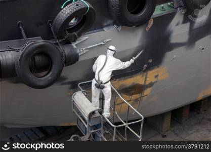 man spray painting hood of ship grey in dock