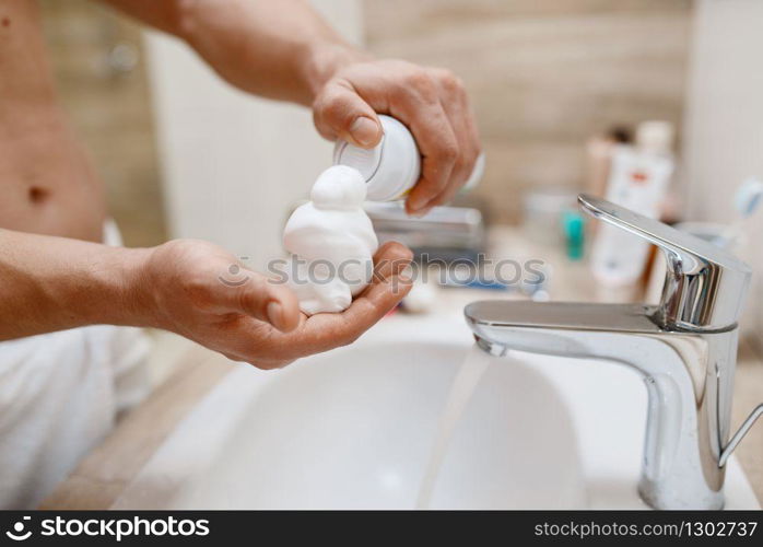 Man squeezes out shaving foam on hand in bathroom, routine morning hygiene. Male person at the sink performs skin and body treatment procedures. Man squeezes out shaving foam on hand, hygiene