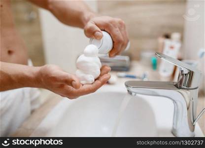 Man squeezes out shaving foam on hand in bathroom, routine morning hygiene. Male person at the sink performs skin and body treatment procedures. Man squeezes out shaving foam on hand, hygiene