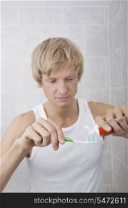 Man squeezing toothpaste on toothbrush in bathroom