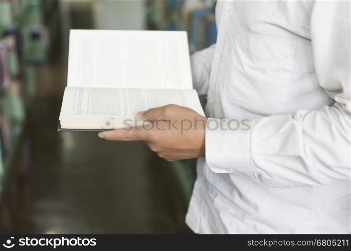 man standing and reading book on floor in aisle in library