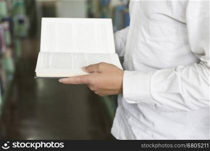 man standing and reading book on floor in aisle in library