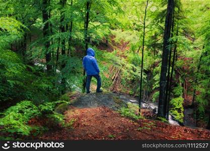 Man standing at the stone in green bright summer rainy forest