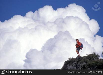 Man Standing Atop Rock With Giant White Clouds in Background