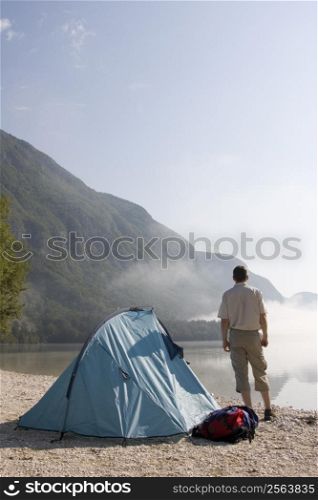 Man standing beside his tent at mountain lake