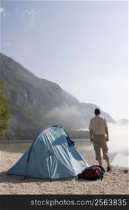 Man standing beside his tent at mountain lake