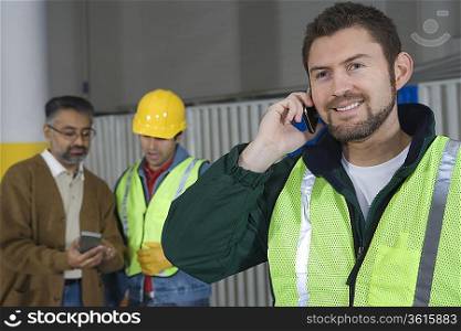 Man standing in factory using telephone colleagues in background
