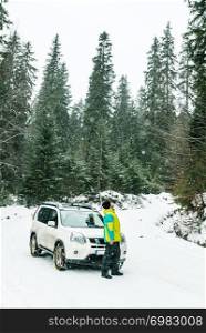 man standing in front of suv car wheels in chains. snowed forest. journey. man standing in front of suv car wheels in chains. snowed forest