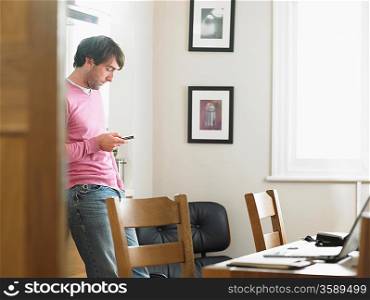 Man standing in kitchen text messaging