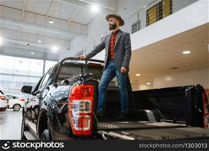 Man standing in the back of new pickup truck in car dealership. Customer in vehicle showroom, male person buying transport, auto dealer business. Man standing in the back of new pickup truck