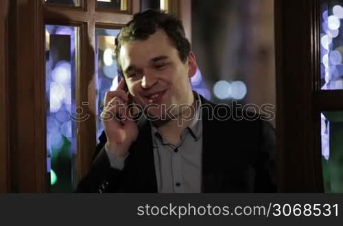 Man standing indoors smiling happily as he chats on his mobile phone, close up view of his face