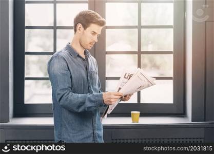 man standing near closed window reading newspaper