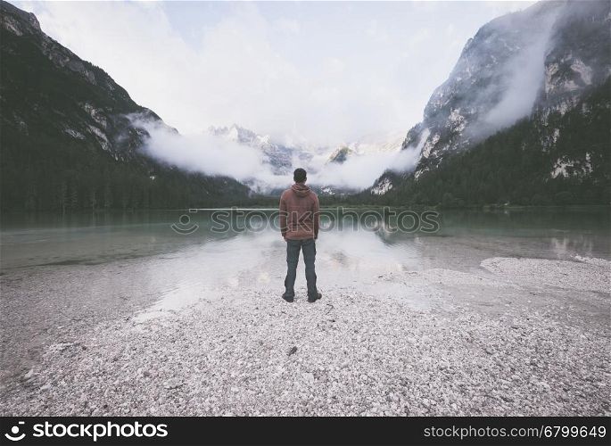 Man standing near mountain lake at cloudy morning