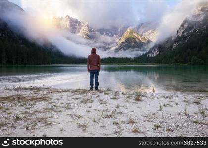 Man standing near mountain lake at cloudy morning