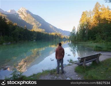 Man standing near the mountain lake at sunny morning