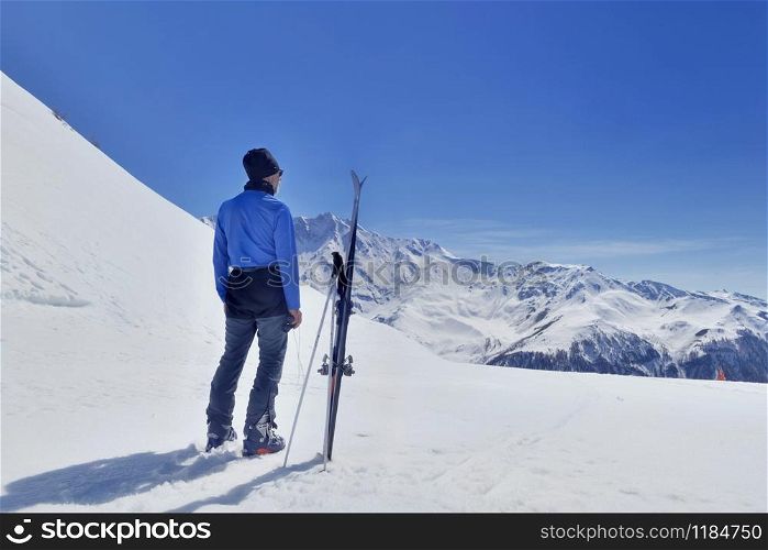 man standing next to ski and looking snowy mountain