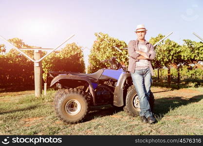 Man standing next to truck in vineyard. Man wearing hat standing next to truck in vineyard