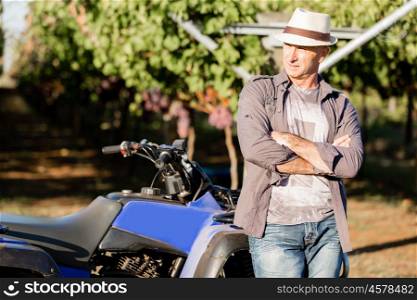 Man standing next to truck in vineyard. Man wearing hat standing next to truck in vineyard