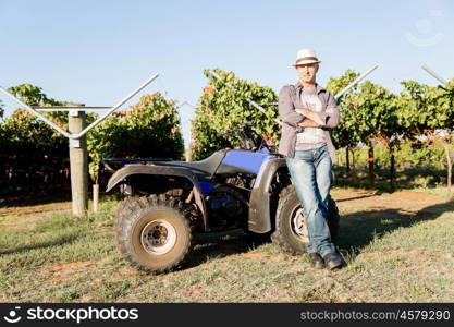 Man standing next to truck in vineyard. Man wearing hat standing next to truck in vineyard