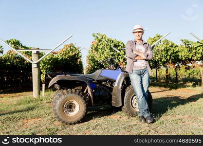 Man standing next to truck in vineyard. Man wearing hat standing next to truck in vineyard