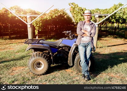 Man standing next to truck in vineyard. Man wearing hat standing next to truck in vineyard