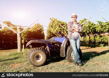 Man standing next to truck in vineyard. Man wearing hat standing next to truck in vineyard