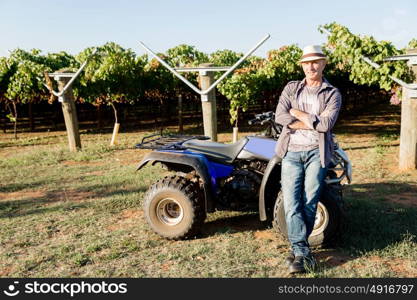 Man standing next to truck in vineyard. Man wearing hat standing next to truck in vineyard