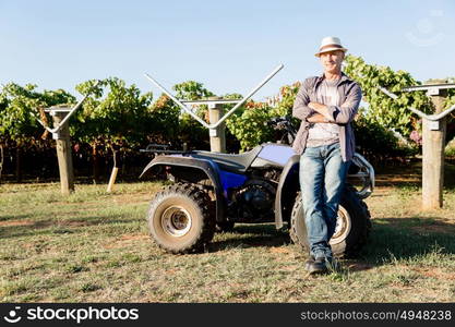 Man standing next to truck in vineyard. Man wearing hat standing next to truck in vineyard