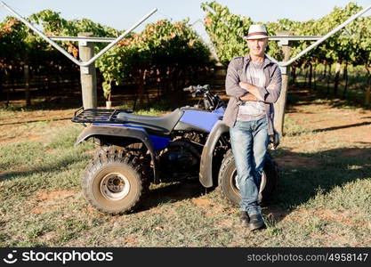 Man standing next to truck in vineyard. Man wearing hat standing next to truck in vineyard