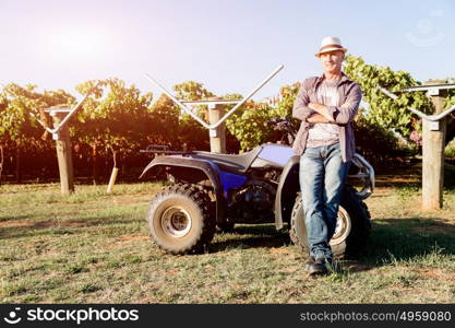 Man standing next to truck in vineyard. Man wearing hat standing next to truck in vineyard