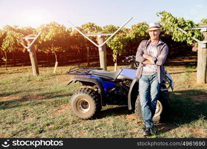 Man standing next to truck in vineyard. Man wearing hat standing next to truck in vineyard