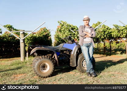 Man standing next to truck in vineyard. Man wearing hat standing next to truck in vineyard