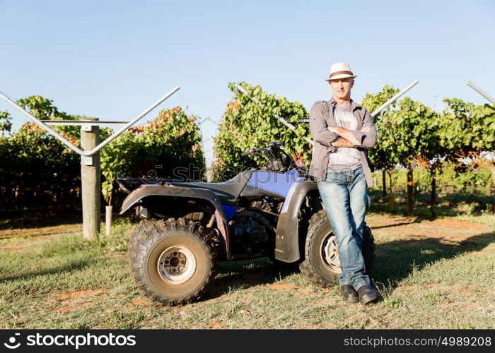 Man standing next to truck in vineyard. Man wearing hat standing next to truck in vineyard