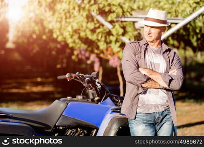 Man standing next to truck in vineyard. Man wearing hat standing next to truck in vineyard