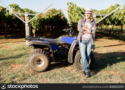 Man standing next to truck in vineyard. Man wearing hat standing next to truck in vineyard