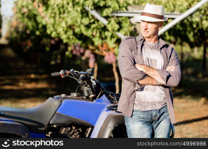 Man standing next to truck in vineyard. Man wearing hat standing next to truck in vineyard