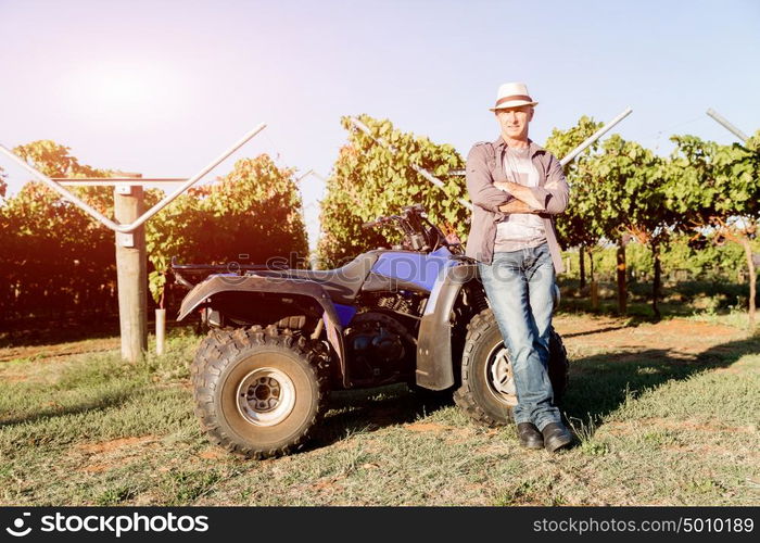 Man standing next to truck in vineyard. Man wearing hat standing next to truck in vineyard